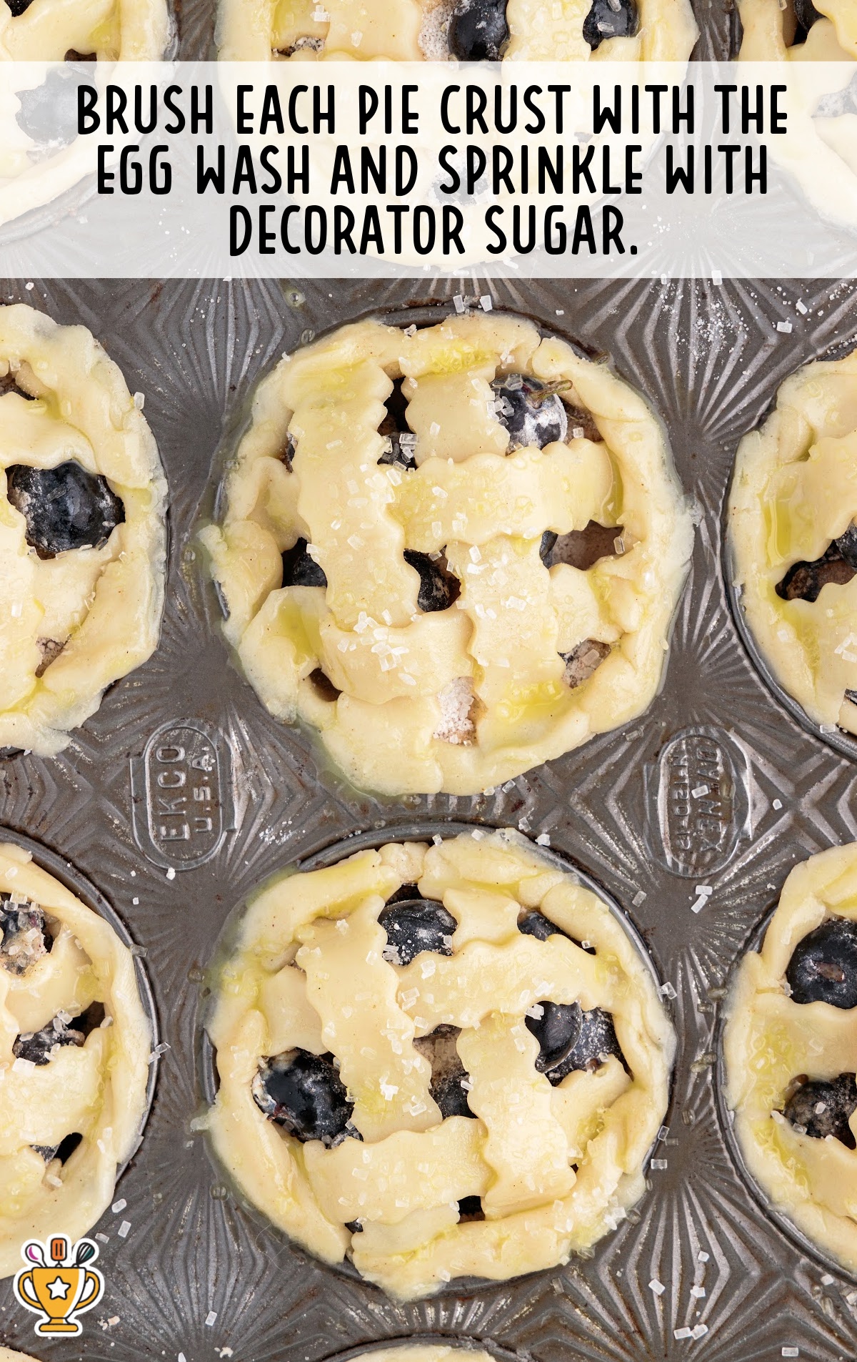 Top-down view of mini pies in the muffin tin, brushed with egg wash and sprinkled with decorator sugar before baking.