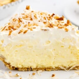 Close-up slice of no-bake coconut cream pie on a white plate with creamy layers and toasted coconut topping.