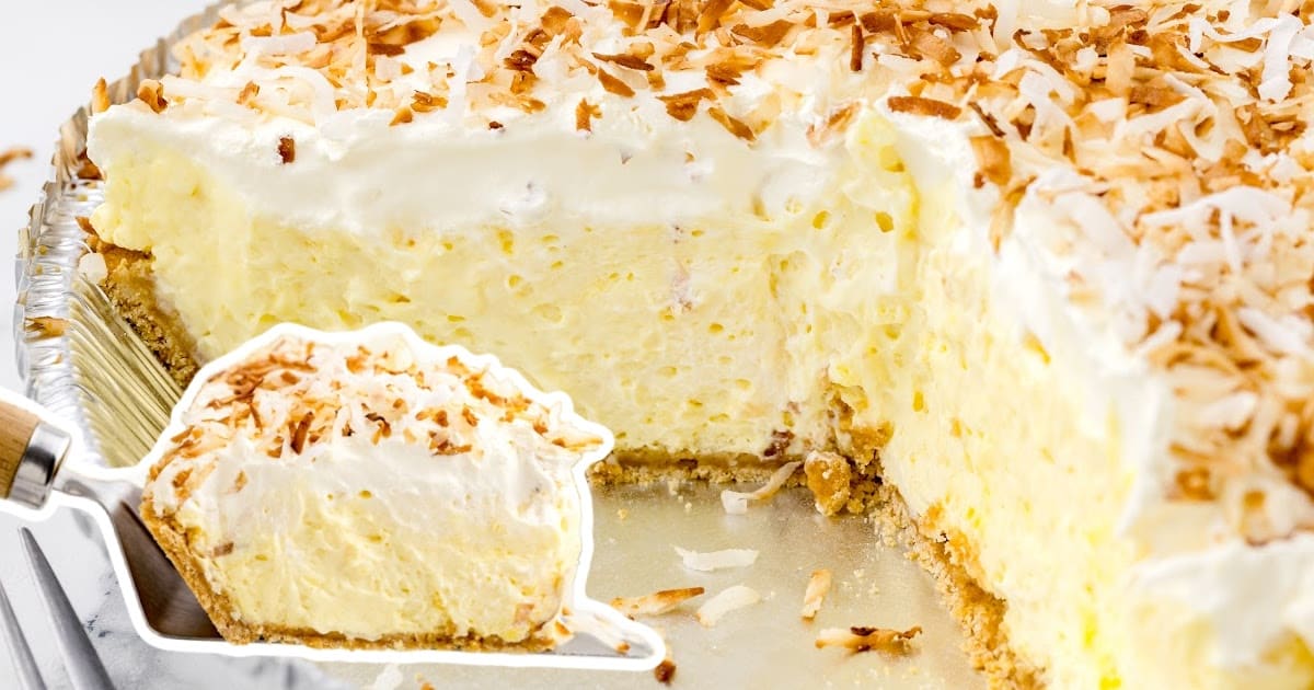 Pie server lifting a slice from a full coconut cream pie, showing thick filling and plenty of golden toasted coconut.