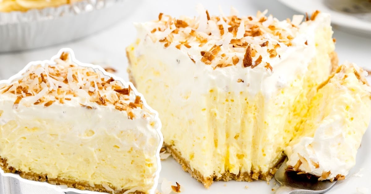 Two large pie slices on a white surface with fluffy coconut topping and a graham crust, one on a server, one on a plate.