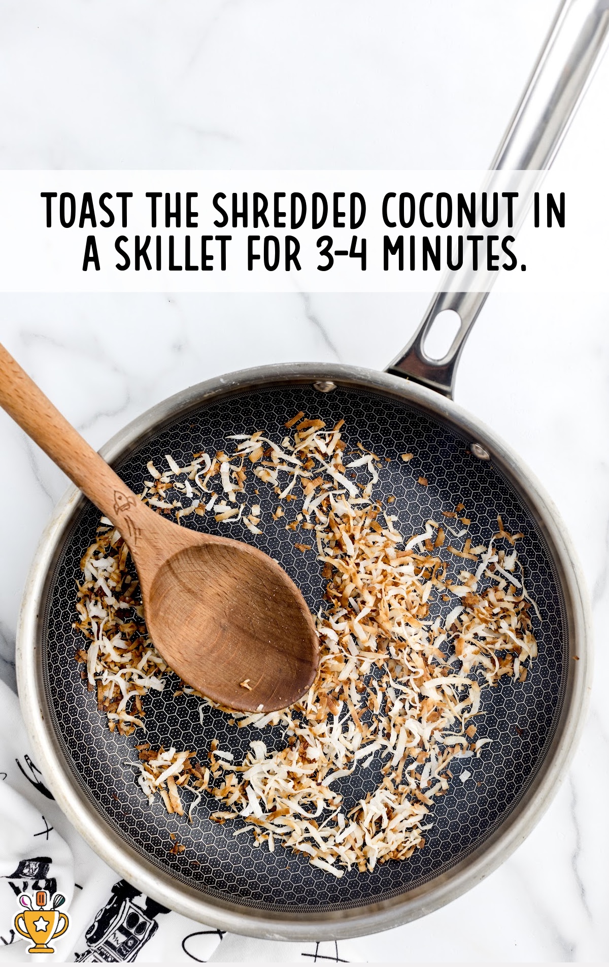 Shredded coconut being toasted in a nonstick skillet with a wooden spoon, showing golden brown flakes and a white background.
