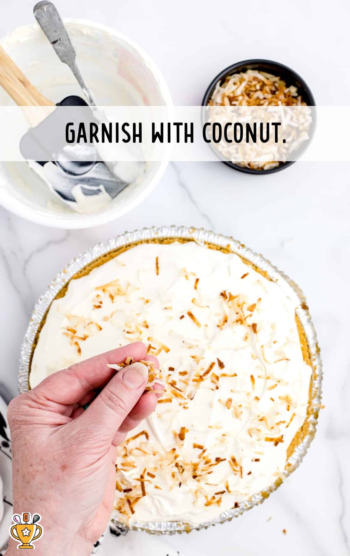A hand garnishing the finished pie with toasted shredded coconut over a white creamy topping.