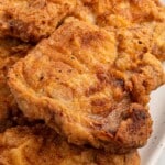 Close-up of crispy fried pork chops with a perfectly fried golden crust, served on a white plate with a fork and knife.