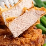 Close-up of a sliced pan-fried pork chop showing the juicy, tender interior with a crispy outer layer, served with green beans.