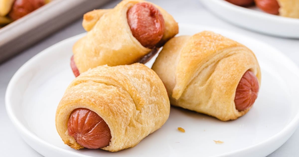 A picture showing pigs in a blanket on a baking tray with a bottle of mustard nearby, perfect for dipping.