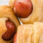 A close-up of pigs in a blanket on a plate, with the text "Pigs in a Blanket" and a smiling pig emoji, highlighting them as a party food.
