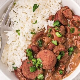 Overhead view of a bowl filled with fluffy white rice and creamy red beans with sausage, garnished with chopped parsley.