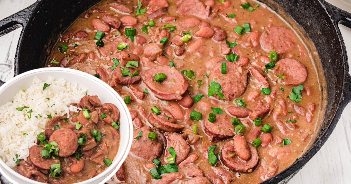 Large cast iron pot filled with simmering red beans and sausage next to a serving of rice in a white bowl.