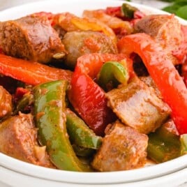 A bowl filled with sausage and peppers featuring red and green bell peppers, onions, and chunks of sausage. The vibrant dish is ready to serve, showcasing a colorful mix of vegetables and meat.