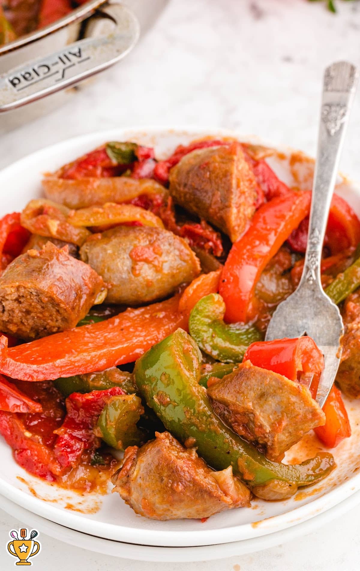 Close-up of sausage and peppers on a plate, featuring sausages, bell peppers, and onions in a savory sauce.