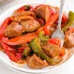 A close-up of a recipe card with ingredients and steps for making sausage and peppers. The recipe is printed clearly, with visuals of the ingredients next to the written instructions.