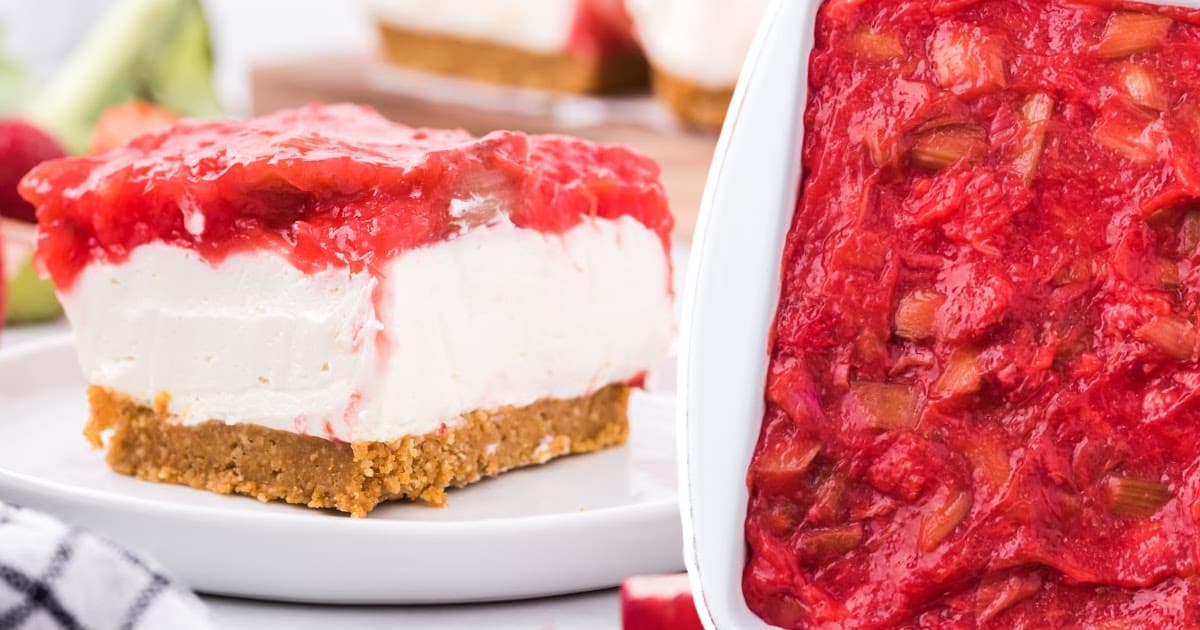 An overhead shot of a slice of strawberry rhubarb cheesecake, featuring the creamy white filling, topped with a mix of strawberries and rhubarb, resting on a golden graham cracker crust.