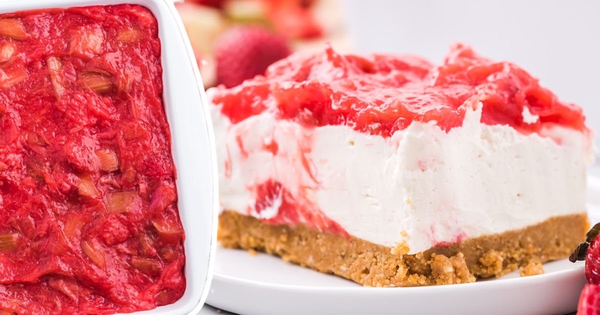 A detailed view of a slice of strawberry rhubarb cheesecake with vibrant red topping made of strawberries and rhubarb, set on a buttery graham cracker crust, garnished with fresh strawberries on the side.