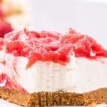 A fresh slice of strawberry rhubarb cheesecake with a crumbly graham cracker crust and a tangy rhubarb and strawberry topping.