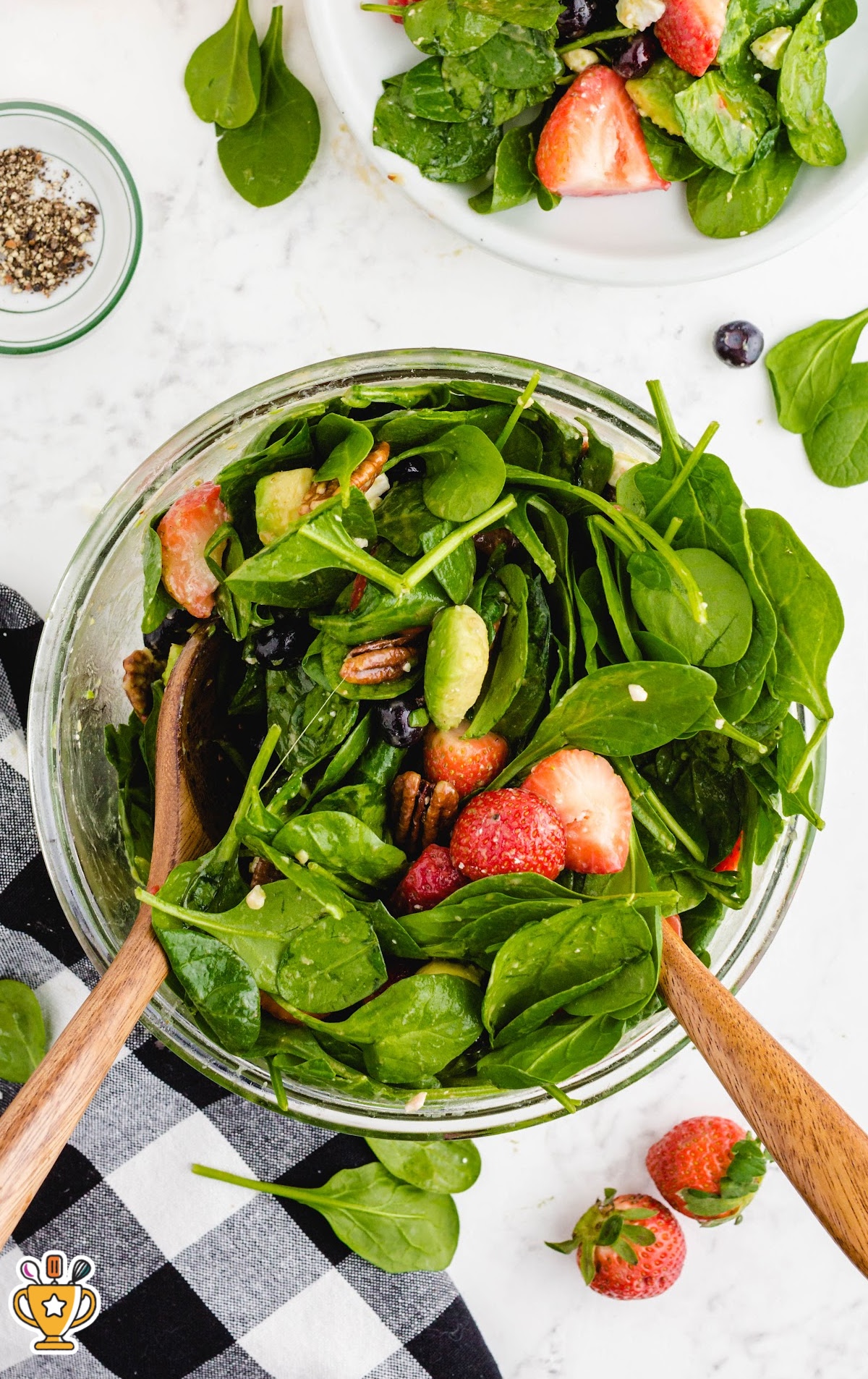 A close-up shot of a strawberry spinach salad with strawberries, spinach leaves, and other colorful ingredients in a clear bowl.
