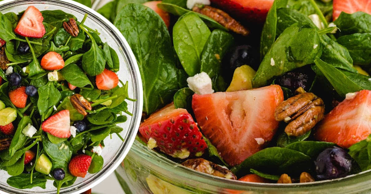 A fresh, colorful strawberry spinach salad with strawberries, blueberries, and spinach, topped with pecans and feta.