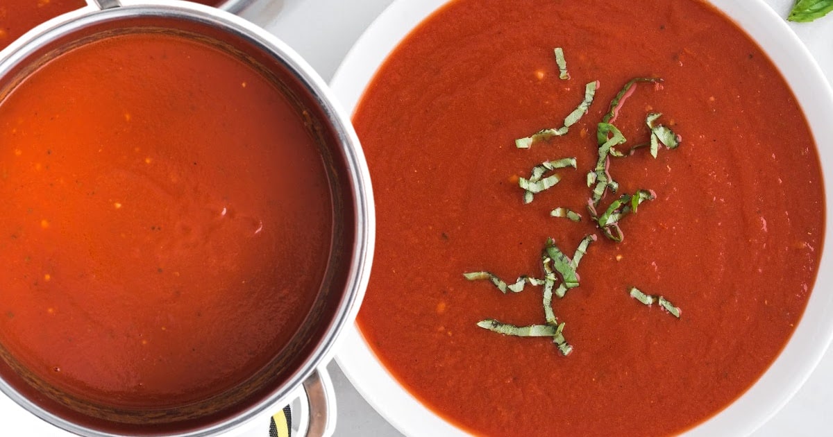 A bowl of freshly made tomato soup with a garnish of basil, alongside a spoon resting in the bowl.