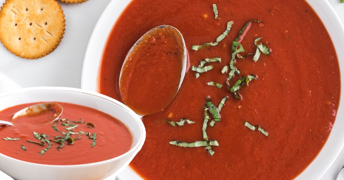 A top-down view of a creamy tomato soup bowl garnished with basil, crackers placed on the side, capturing a comforting meal.