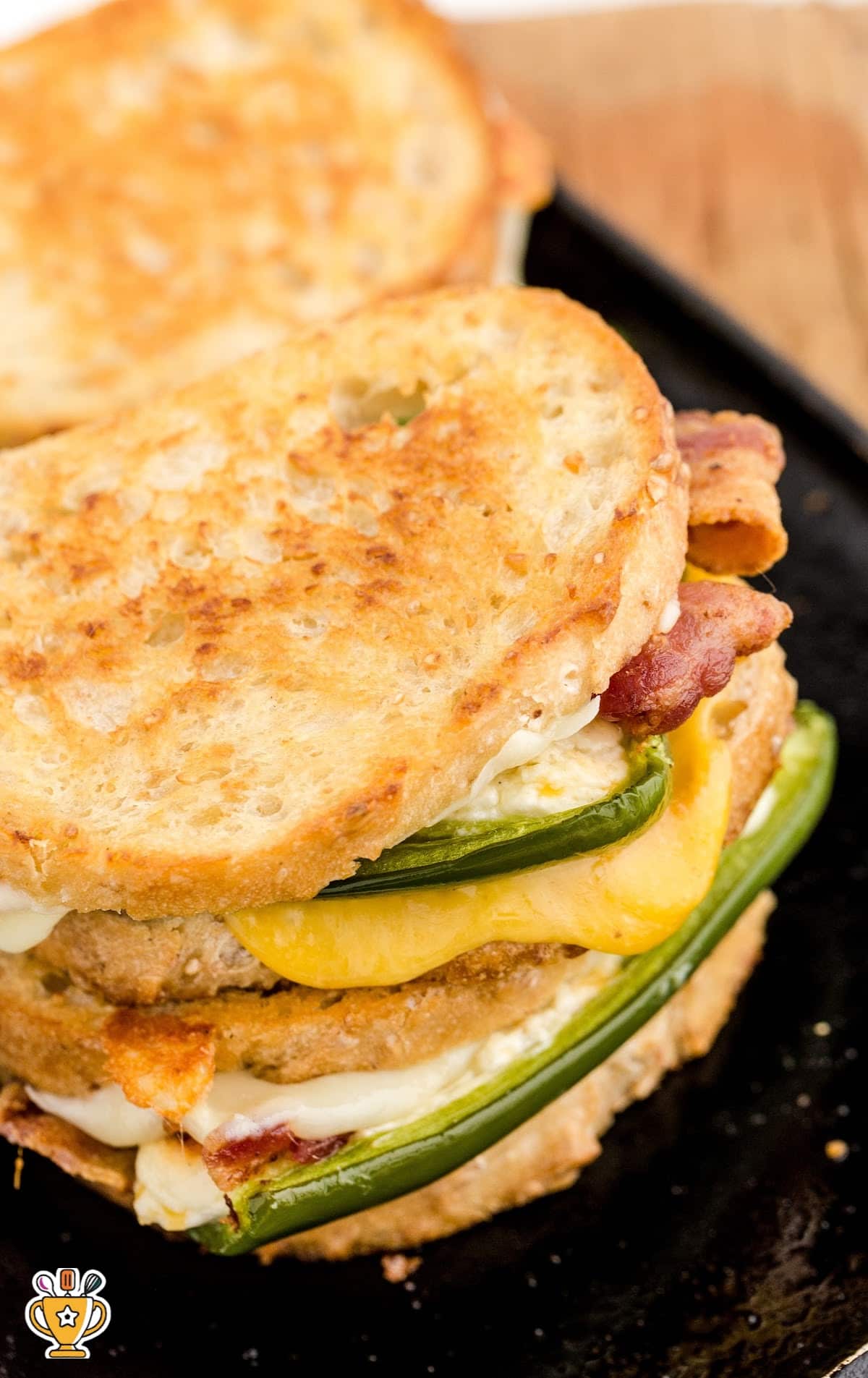 Golden-brown grilled sandwich on a skillet filled with jalapeños, bacon, and melted cheddar and mozzarella.