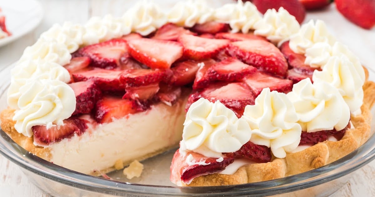 A strawberry cream cheese pie with a generous layer of fresh strawberries, surrounded by whipped cream swirls on the crust's edge.