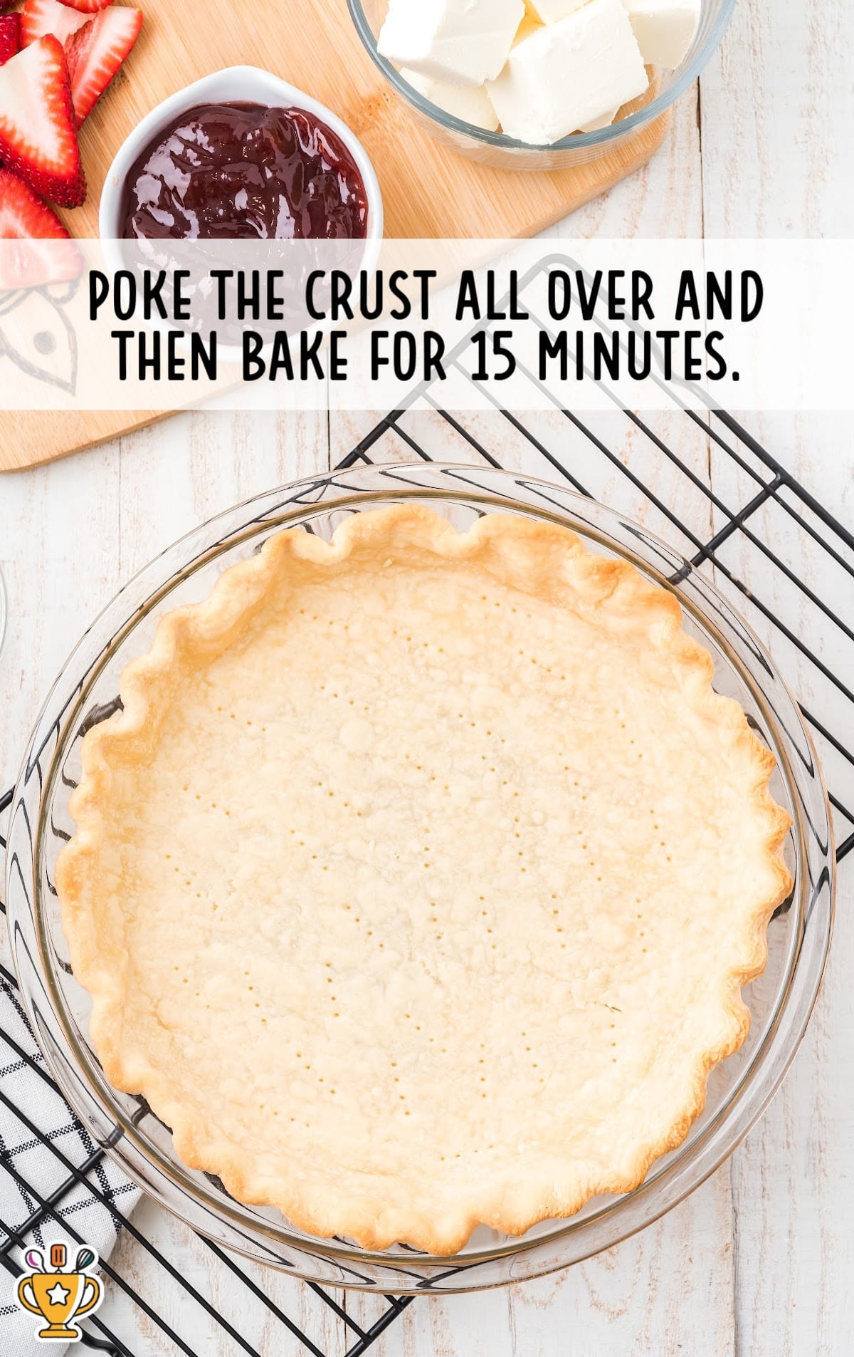 A pre-baked pie crust, strawberries, cream cheese, strawberry jam, and other ingredients laid out on a kitchen counter.