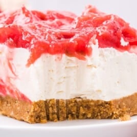 A close-up view of a piece of strawberry rhubarb cheesecake topped with a vibrant mixture of strawberries and rhubarb. The smooth, creamy filling contrasts beautifully with the crunchy graham cracker crust.