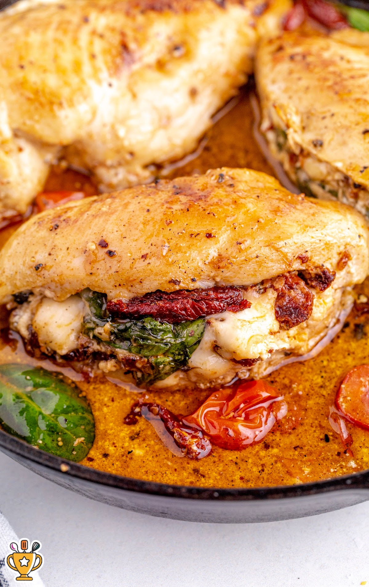 A skillet with stuffed chicken breasts filled with spinach, sun-dried tomatoes, and cheese, swimming in a savory sauce.