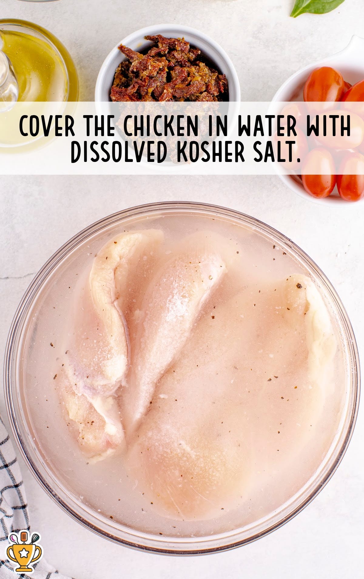Chicken breasts being brined in a bowl of water with dissolved kosher salt, a step in preparing the chicken.
