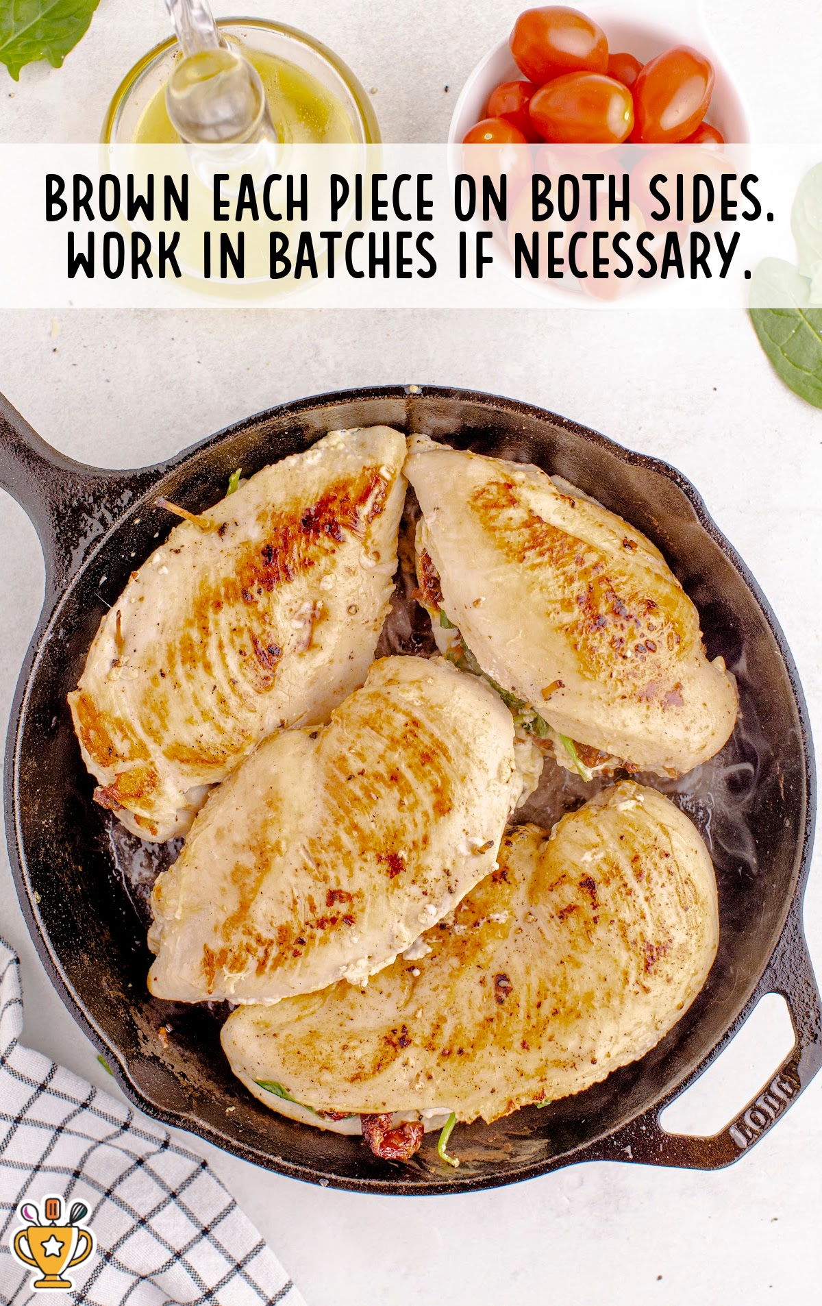A skillet with browned chicken breasts, stuffed with sun-dried tomatoes and spinach, ready to be baked until fully cooked.