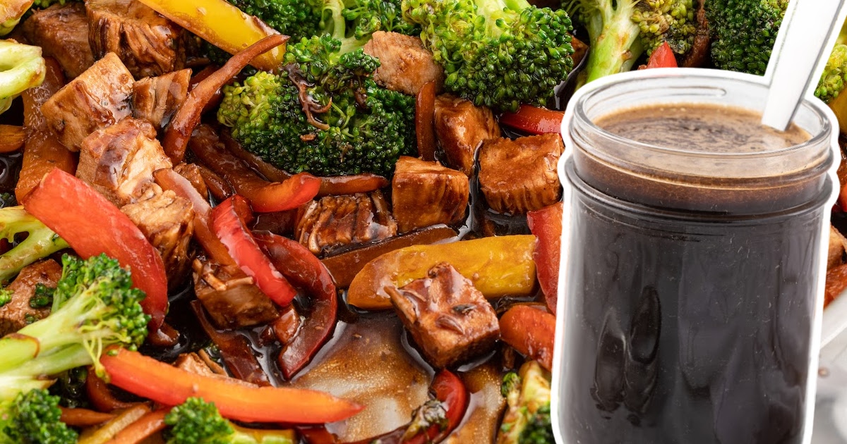 Close-up of a colorful vegetable stir fry with broccoli, red and yellow bell peppers, tofu cubes, and carrots coated in a glossy dark sauce, with a glass jar of thick, dark stir fry sauce and a spoon in the foreground.