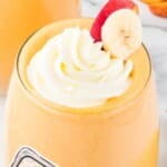 Vertical image of peach banana smoothie in a glass with whipped cream, banana, and peach slices, plus blender ingredients and text overlay saying 'Super Creamy Banana Peach Smoothie.'