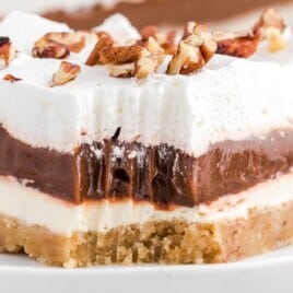 Close-up side view of chocolate delight on a white plate with distinct pudding, cream cheese, and whipped layers.