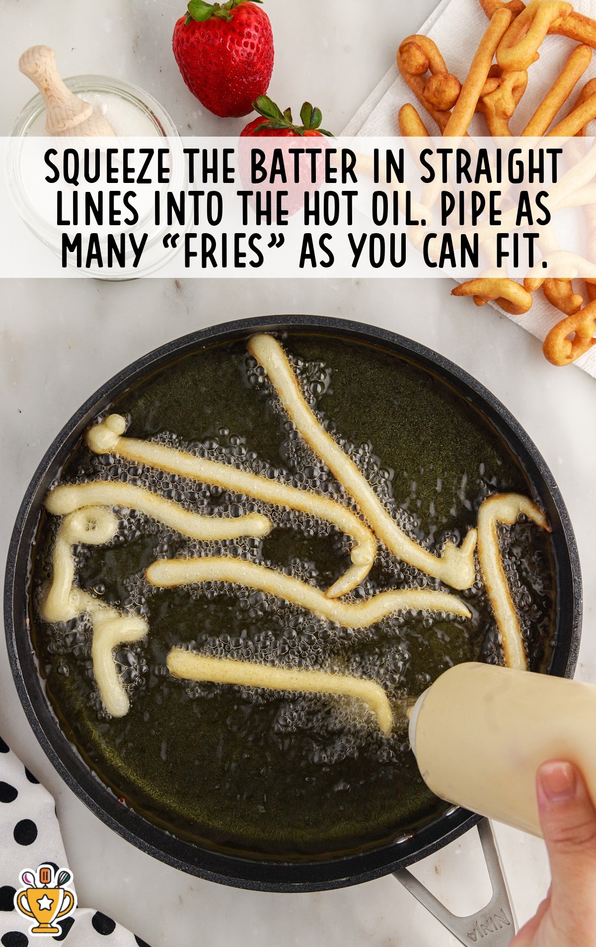 Raw funnel cake batter being piped into hot oil in squiggly lines to form fries using a squeeze bottle.