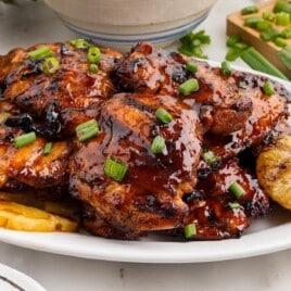 Plate of grilled Huli Huli chicken thighs glazed in sauce, served with grilled pineapple slices and garnished with green onions.