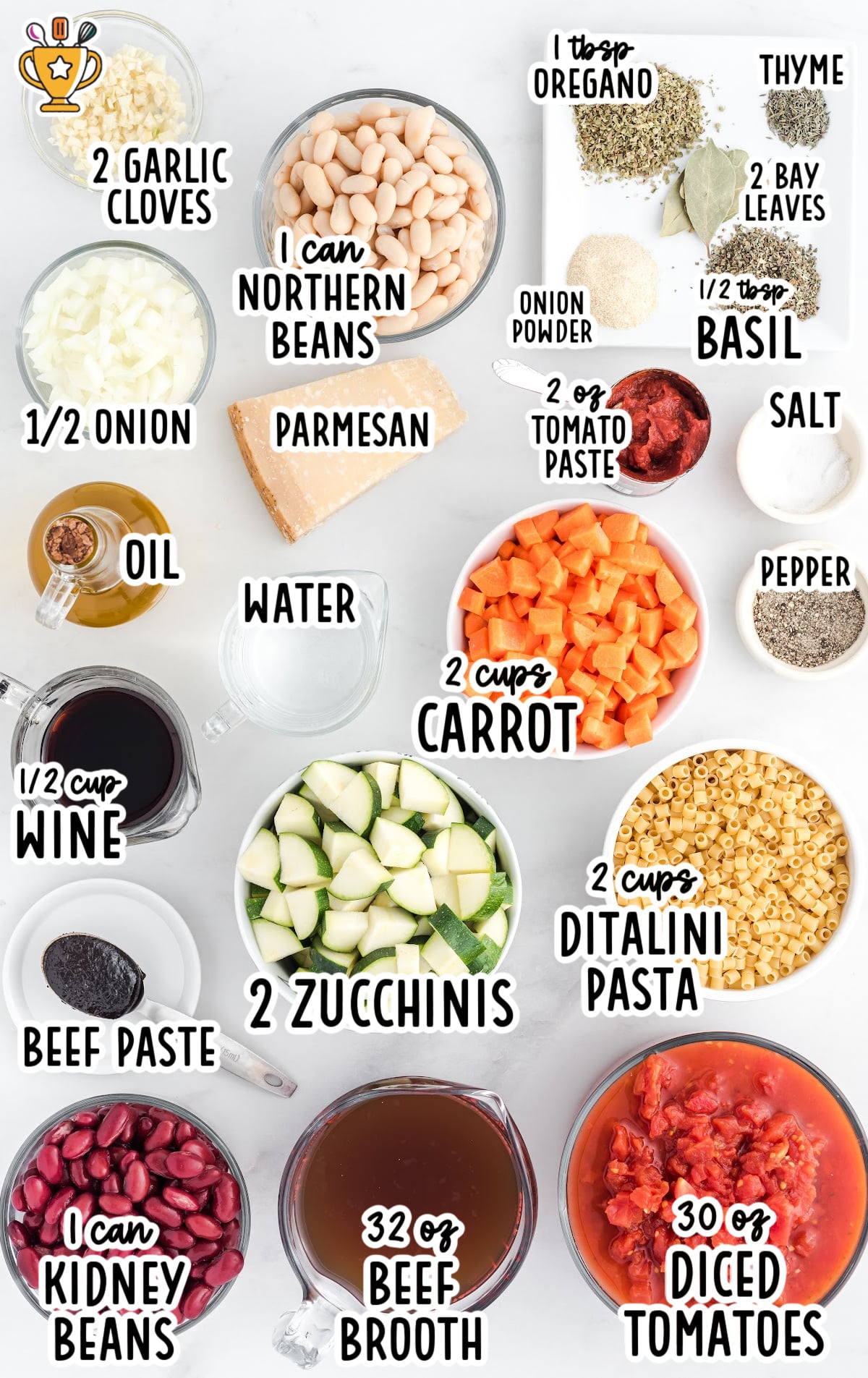 An overhead view of all the fresh and pantry ingredients for minestrone soup neatly arranged on a white surface.