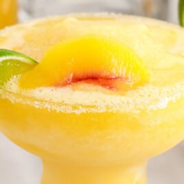 Bright and refreshing peach margarita garnished with a lime slice and served over ice in a cocktail glass