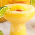 Bright and refreshing peach margarita garnished with a lime slice and served over ice in a cocktail glass