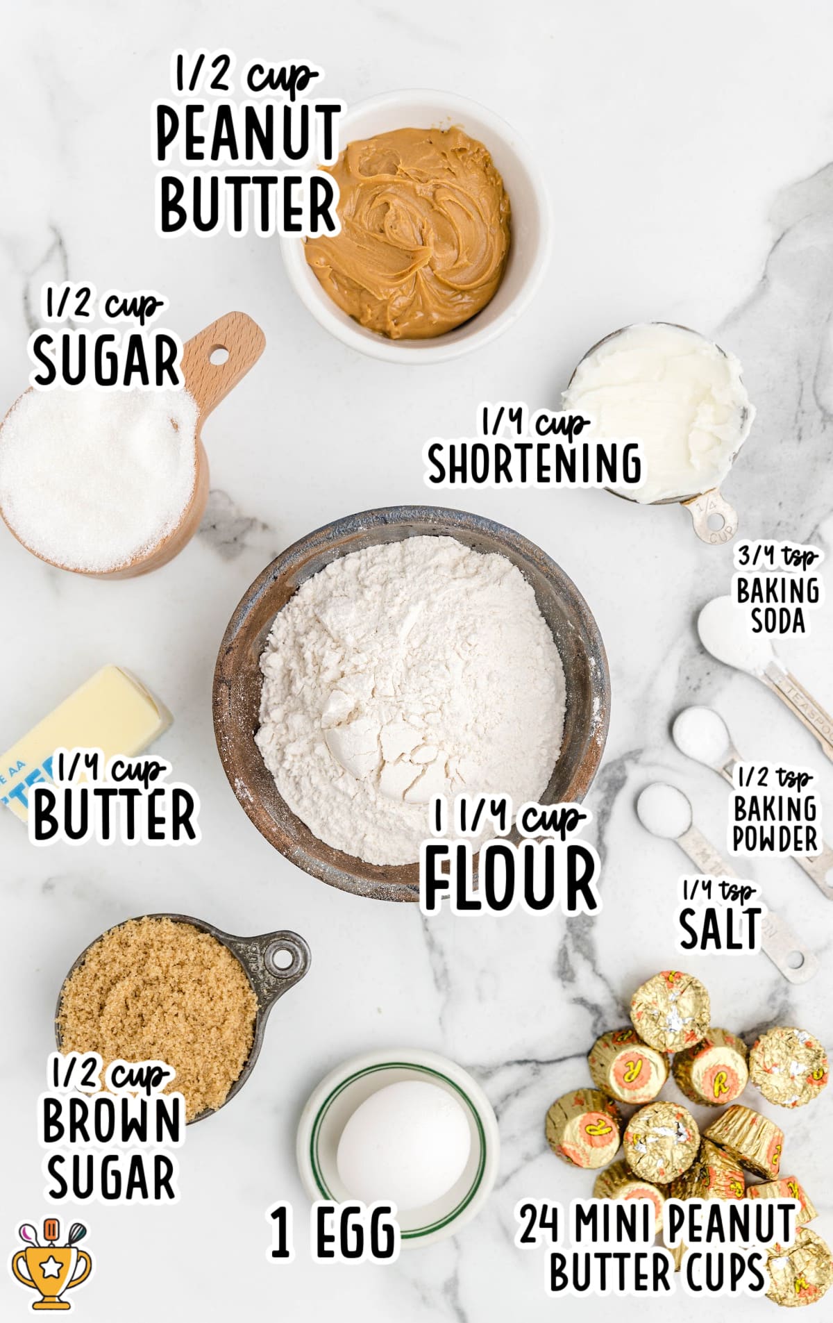 A white surface filled with labeled ingredients for peanut butter cookie cups, including cookie dough, peanut butter cups, and a muffin pan.