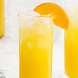 Tall glass of orange Screwdriver cocktail with ice and an orange slice garnish, set against a bright white background.