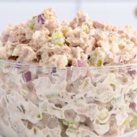 Glass bowl filled with chunky tuna salad, showing chopped red onions and celery mixed with creamy dressing on a white countertop.