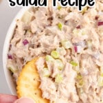 A creamy tuna salad with diced red onions and celery in a white bowl, served with a round buttery cracker.