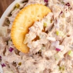 Overhead view of creamy tuna salad with red onions and celery in a white bowl, served with round crackers on the side.