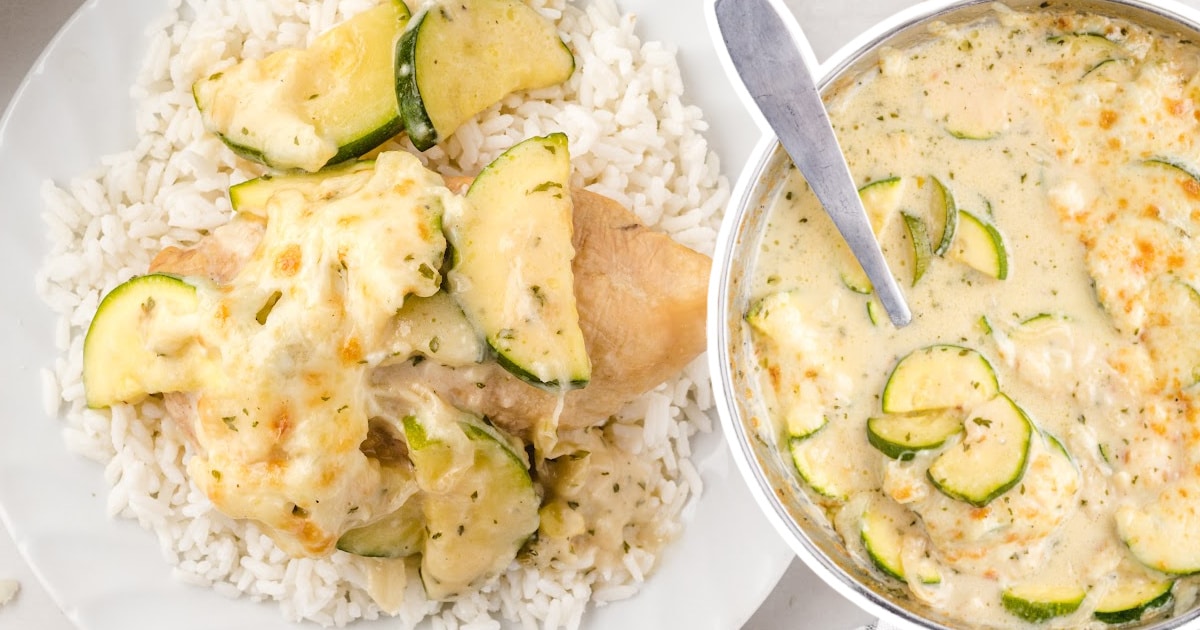 Top-down view of cheesy zucchini gratin on a dinner plate with white rice and a serving spoon in the pan beside it.