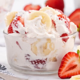 Strawberry banana cheesecake salad with Cool Whip and creamy filling in a white bowl, garnished with fresh sliced fruit