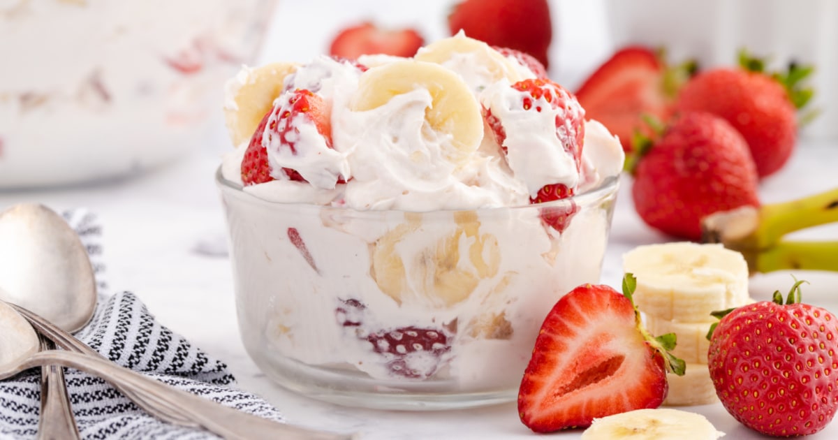 Strawberry banana cheesecake salad with Cool Whip and creamy filling in a white bowl, garnished with fresh sliced fruit