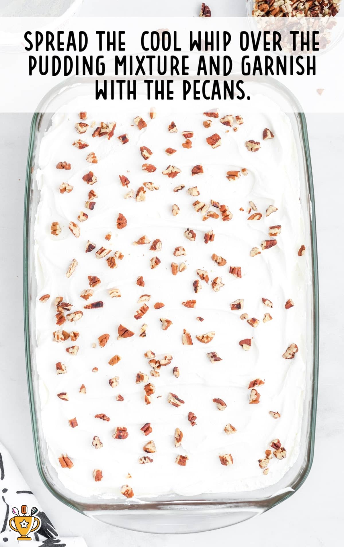 Finished dessert in a glass dish topped with Cool Whip and sprinkled with chopped pecans, ready to chill and serve.