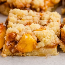 Overhead view of sliced peach bars on parchment, showing buttery crust, juicy peach filling, and crumbly golden topping ready to serve.