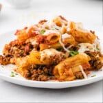Plate of baked ziti with rigatoni noodles, ground beef, tomato sauce, and melted cheese, ready to eat and garnished with parsley.