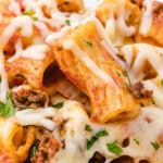 Close-up of cheesy baked ziti with ground beef, marinara sauce, and melted mozzarella served from a crockpot, garnished with parsley.