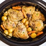 Slow cooker filled with golden brown chicken thighs, baby carrots, and potatoes, perfectly cooked and garnished with fresh parsley.